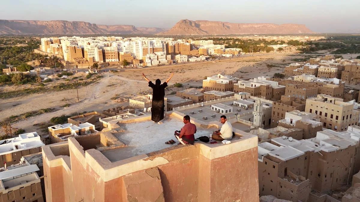 Travelers overlooking the mudbrick skyline of Shibam from a traditional tower-house rooftop
